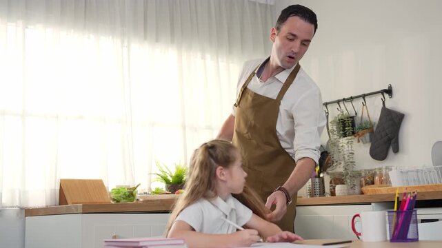 Happy single father assisting daughter with school work while cooking in home kitchen