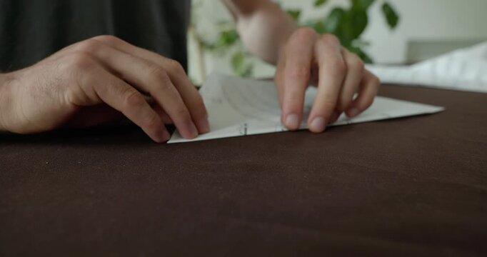 Close-up male hands fold sheet of paper making paper airplane. 4K 10-bit