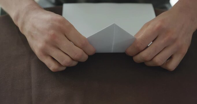 Close-up male hands fold sheet of paper making paper airplane. 4K 10-bit