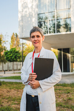 Portrait of mature woman doctor hold clipboard in front hospital park