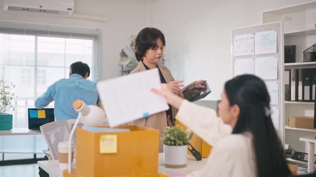 Sad Asian businesswoman packing her personal belongings into a cardboard box after being laid off from her job, representing job loss, unemployment, economic crisis, and career failure.