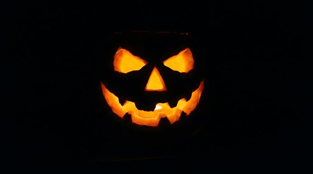 Glowing jack-o-lantern pumpkin carved with a spooky face illuminated by internal fire against black background