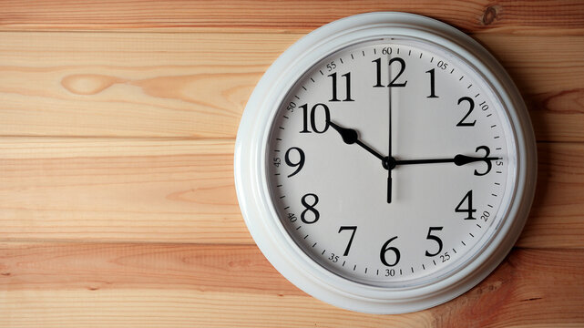White wall clock showing quarter past ten on a wooden background