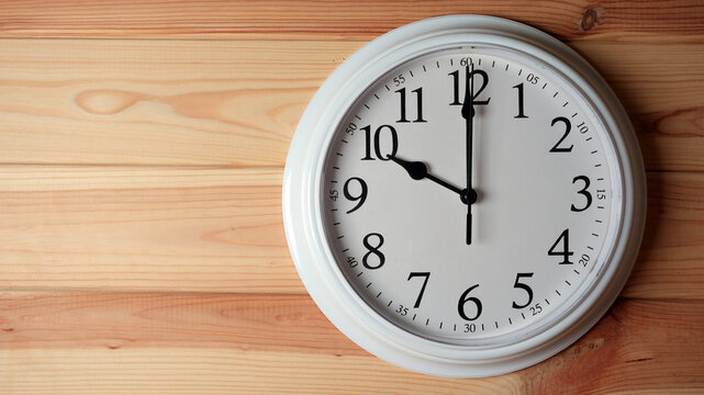 White wall clock showing ten o clock on a wooden background