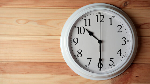 White wall clock showing half past ten on a wooden background