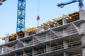 Voronezh, Russia, July 23, 2026: Tower cranes over the construction site of a monolithic multi-story residential building  scaffolding covered with netting. © Beliakina Ekaterina