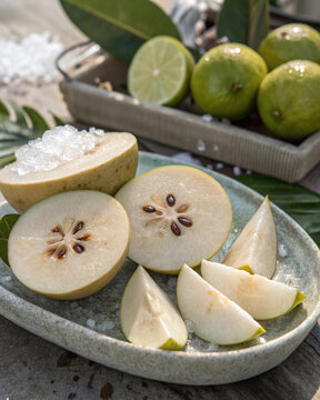 Premium white sapote halves with creamy flesh, glossy seeds, condensation, tropical leaves, lime zest and crushed ice accents