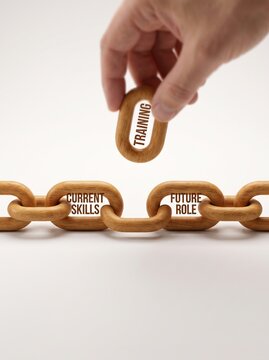 Hand inserting a wooden chain link labeled training to connect current skills and future role, representing the concept of closing the skills gap through upskilling