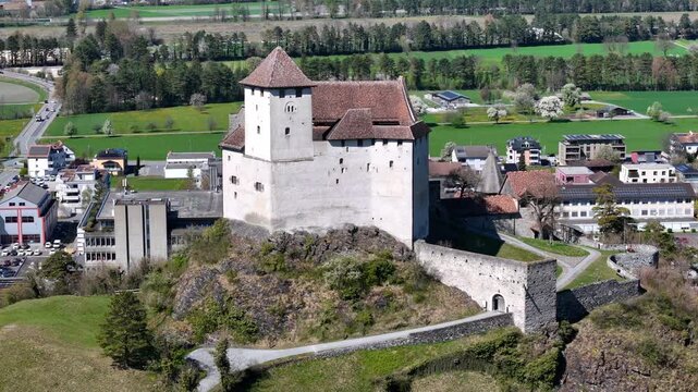 modern office building gutenberg castle round tower close orbit gatehouse defensive walls stone rocky outcrop hilltop balzers town rooftops road curving parked cars liechtenstein heritage site