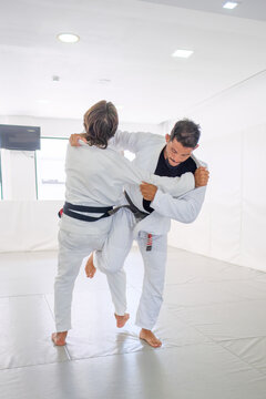 Two male martial artists enter uchi-mata, the judo inner thigh reaping throw, during Brazilian jiu jitsu (BJJ) practice as the active leg rises against the inner thigh