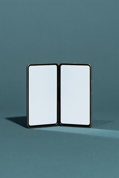 Clamshell foldable phone standing as a wedge on a sage background, featuring blank white screens for a device mockup and copy space