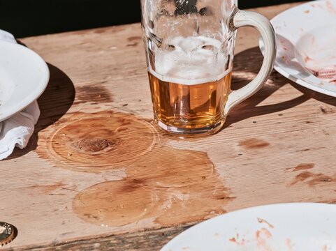 Stoneware beer stein on a weathered timber table with wet rings and foam, a rustic scene for brewery and festival brands