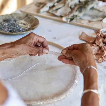 Hands sewing intricate beadwork on a hoop with waxed thread and hide, a detailed craft process for maker platforms and cultural heritage