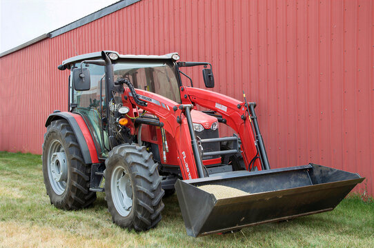 IRRICANA, CANADA - 08 AUGUST 2026: Red Massey Ferguson tractor with a front loader bucket parked near a red barn.