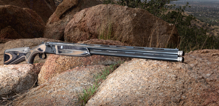 Over-under 12 gauge shotgun resting on boulders on a mountainside