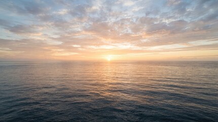 Obraz premium The sun rises over the ocean, casting a warm glow on the water and sky. Clouds are scattered across the horizon, reflecting the colors of the sunrise.