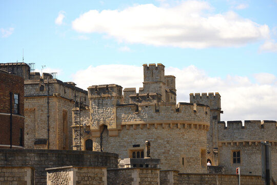 This image shows the historic stone walls and towers of a medieval castle under a bright blue sky with soft white clouds, capturing architectural details like battlements and windows