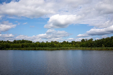 Obraz premium Wide angle view of a calm lake and river landscape with reed shores under a cloudy blue sky