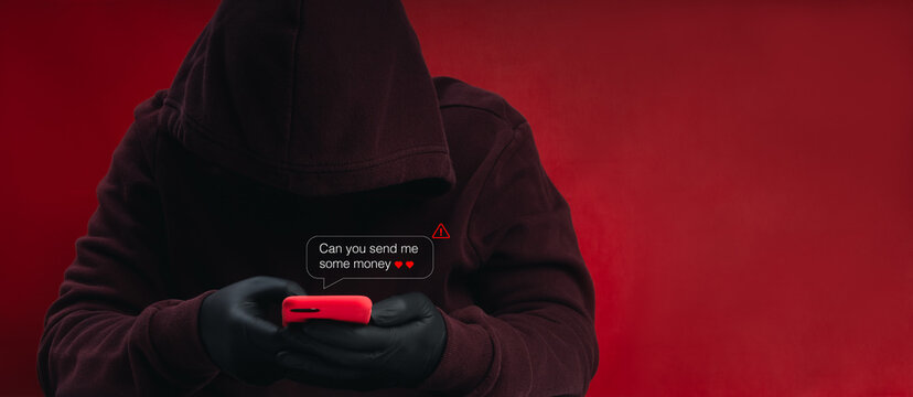 Hooded anonymous scammer in black gloves uses smartphone to send romantic money request. Online dating fraud, romance scam, social engineering, financial manipulation and digital safety risks concept.