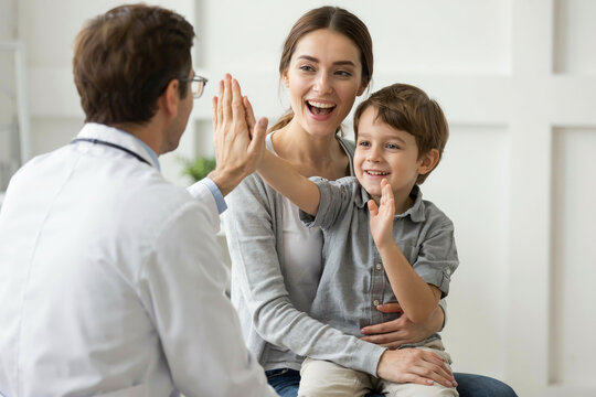 Doctor high-fiving child and mother in medical office.