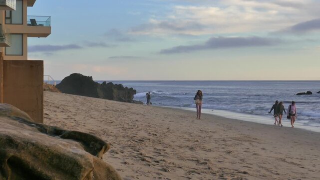 Looking north up the coast from Oak Street Beach at Laguna Beach, California during dusk. Tourists and other beach goers walking on the sands.