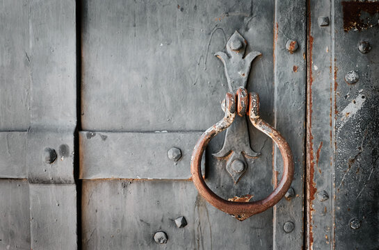 Close-up of an antique weathered metal door with a decorative iron door knocker, rivets, rust and textured surface.