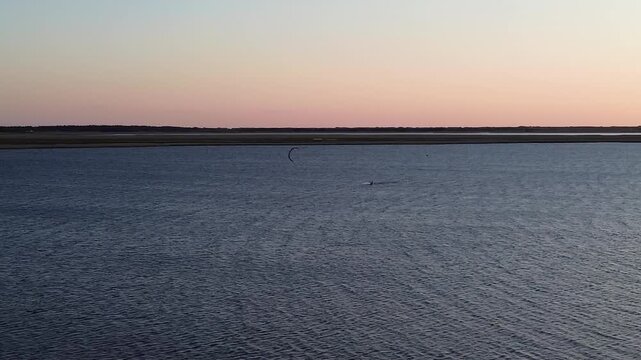 Drone aerial view of a kitesurfer performing an impressive jump over calm fjord water during a vibrant sunset in Bork Havn