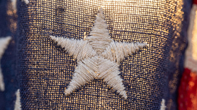 Close up embroidered star on the American flag with warm golden sunlight highlighting fabric texture, evoking patriotism, pride, freedom and hopeful celebration