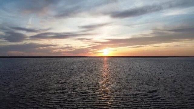 A serene drone video capturing the golden hour sunset over Bork Havn, Denmark. The camera hovers steadily, facing the setting sun over the calm Ringk&oslash;bing Fjord, before smoothly panning left to reveal