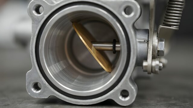 Close-up of a metallic engine throttle body with a butterfly valve and spring