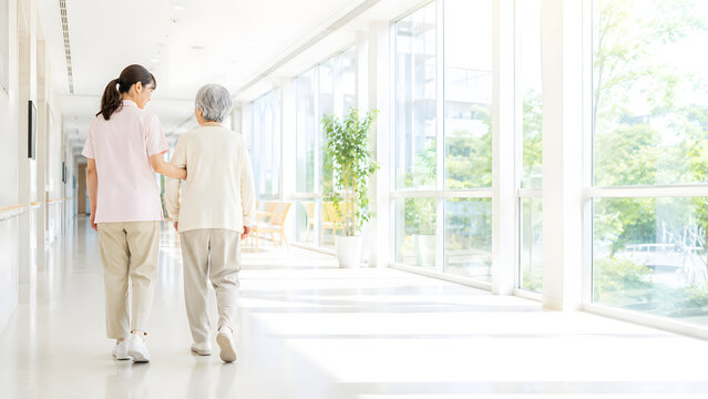 Caregiver walking with an elderly woman in a bright care facility