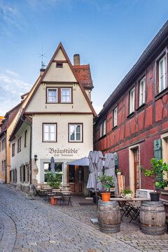 Rothenburg ob der Tauber, Germany - September 2, 2025: Charming Cobblestone Street with Historic Half-Timbered Buildings and Outdoor Cafe Seating in a Traditional German Town