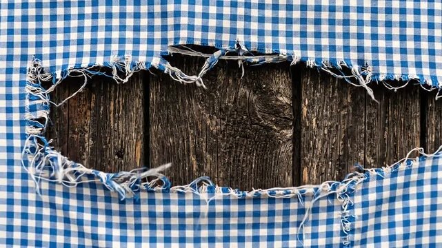 Blue and white checkered fabric with a large tear revealing dark rustic wooden planks underneath