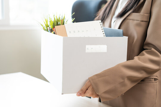 Unemployed, quite job. Desperate asian young businesswoman resigning from company, hand holding cardboard, packing belongings, stuff into box, layoff or changing work. Resignation, employment concept.