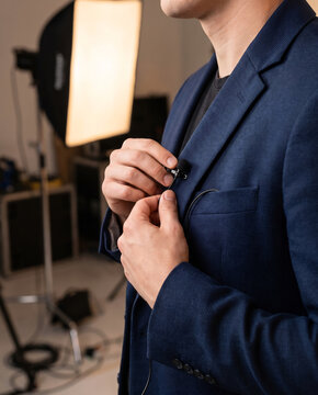 Hands clipping a lavalier microphone onto a blazer lapel before an interview