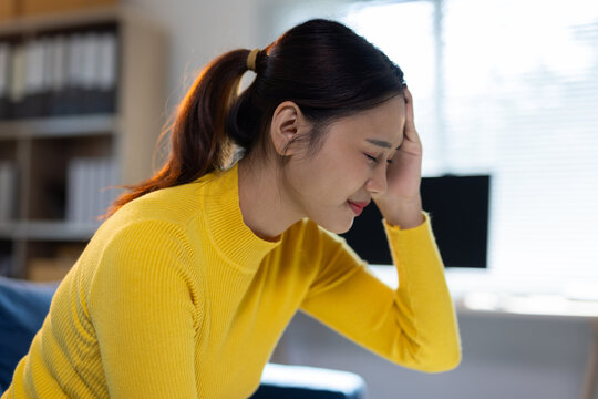 Young woman suffering from headache pain and stress. Young Asian woman experiencing severe headache and migraine, holding her head, feeling tired and stressed.