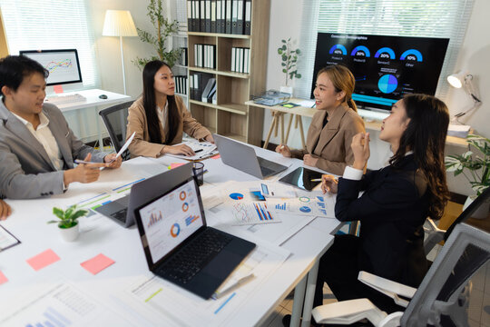 Business team analyzing data during office meeting. Asian business professionals collaborating in office, analyzing financial data and charts.