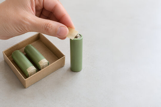 Hand Applying Nonconductive Tape to a Used AA Battery Terminal Before Safe Recycling