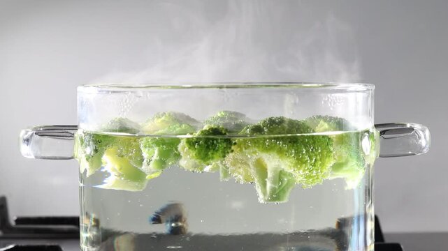 Boiling broccoli in a glass pot on the stovetop with steam rising