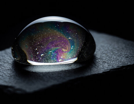 Macro Water Droplet with Iridescent Cosmic Oil Sheen on Dark Slate Stone