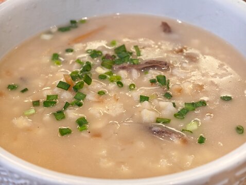 Close-up traditional Xi'an style pita bread soaked in lamb soup (Yangrou Paomo) in a white bowl, garnished with green onions.