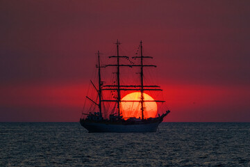 ⁠Sailing tall ship silhouette in front of giant red rising sun at sea horizon © Cornelia