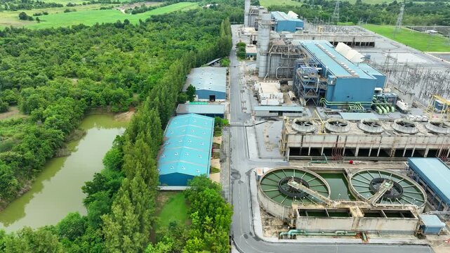 Aerial perspective of a modern power plant bordered by dense green forest, representing reliable electricity supply, industrial development, energy security and environmental responsibility.
