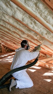 Worker applying spray foam insulation in attic for energy efficiency