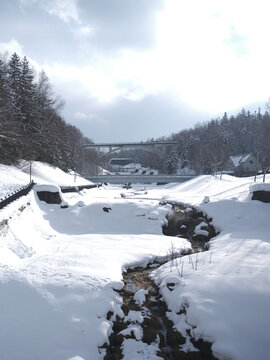 Snow-covered river valley with stream conifers and bridge Hokkaido