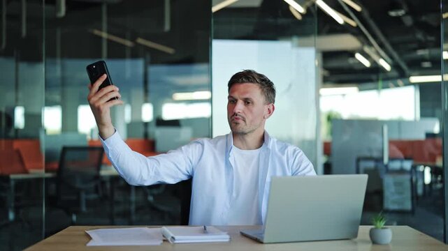 Frustrated bearded businessman in blue shirt looking for mobile network signal, waving smartphone in air while experiencing internet connection loss and poor cellular reception in office.
