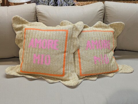 Vista de cerca con un sof&aacute; con asiento y respaldo tapizados en tela, con cojines con texto bordado Amore Mio, en una tienda de muebles	