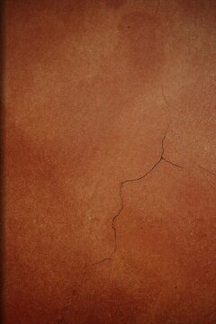 Close up of a textured terracotta wall surface with a prominent crack running through the center