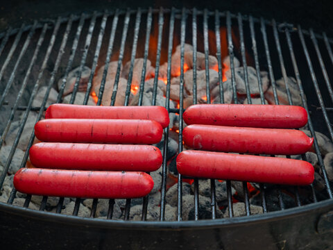 Red hot dogs cook over hot coals on an outdoor grill