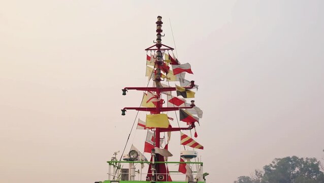 BANJARMASIN, INDONESIA - SEPTEMBER 15, 2026: A close-up view of a ship's mast adorned with colorful international maritime signal flags under a sky with light morning mist. 4K